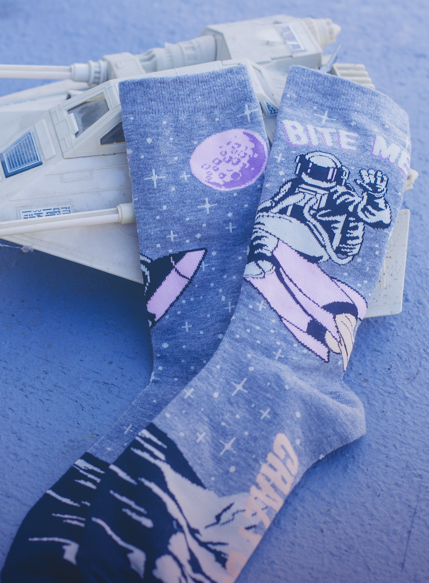 Blue socks with an astronaut riding a spaceship design, placed on top of a toy spaceship  
