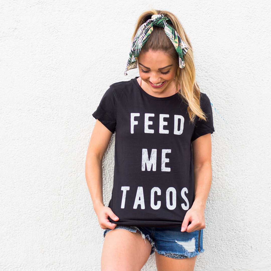 Woman looking at her black feed me tacos printed shirt