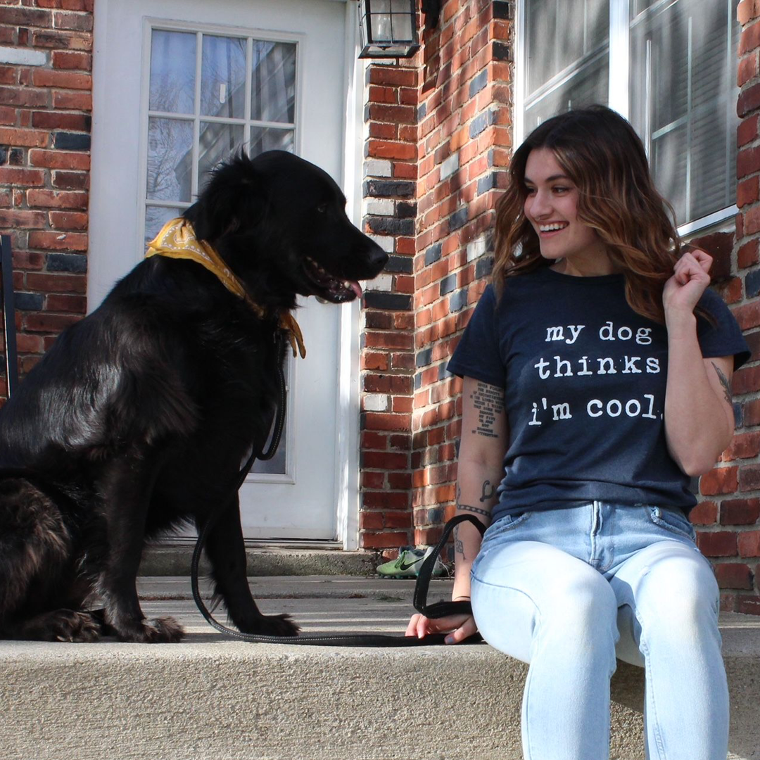 Woman looking at her black dog wearing a my dog thinks I'm cool navy blue printed shirt