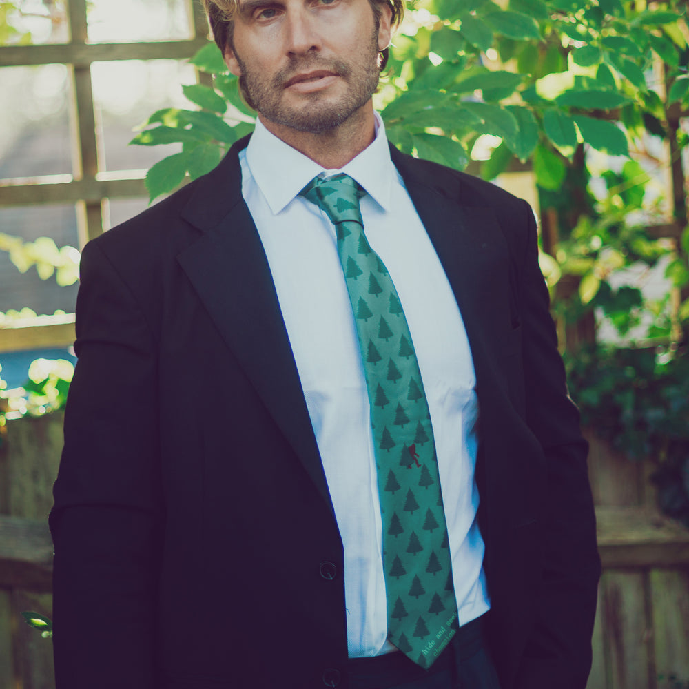 Man wearing a dark suit and green patterned tie outdoors with plants in the background